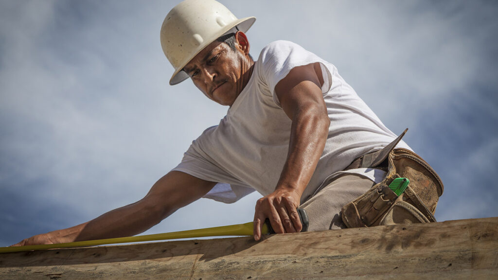 A Hispanic construction worker on a residential construction site in Southwest Florida. He is on top the top of a concrete wall forming part of the shell of the building.