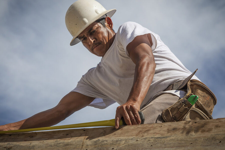 A Hispanic construction worker on a residential construction site in Southwest Florida. He is on top the top of a concrete wall forming part of the shell of the building.
